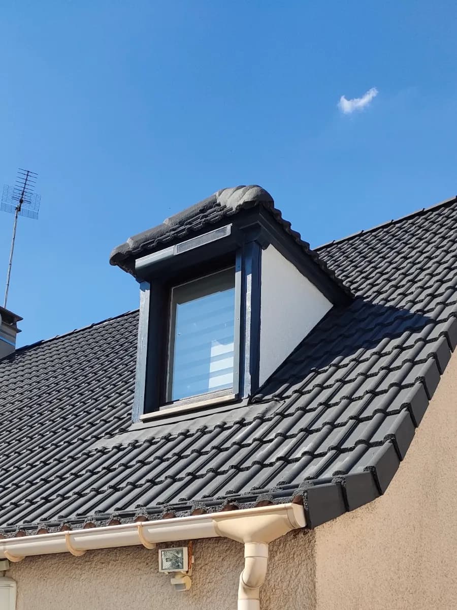 Toiture en tuiles béton nettoyée et recolorée anthracite par Artisans L.L, lucarne aux joues blanches, ciel bleu